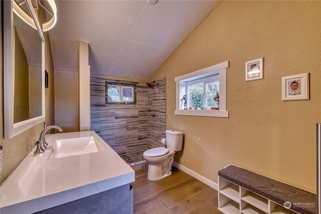 bathroom featuring toilet, a tile shower, lofted ceiling, wood-type flooring, and sink