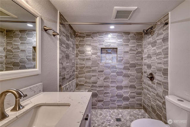 bathroom with a textured ceiling, tiled shower, vanity, and toilet