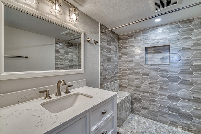 bathroom featuring a textured ceiling, tiled shower, and vanity