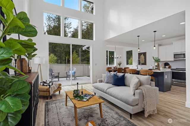 living room featuring sink, an inviting chandelier, a towering ceiling, and light wood-type flooring