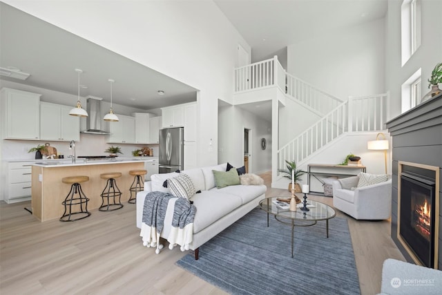 living room featuring a towering ceiling, sink, and light wood-type flooring