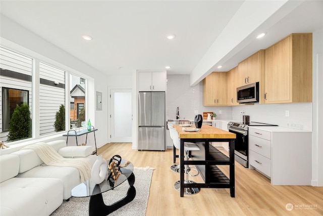 kitchen with light hardwood / wood-style flooring, decorative backsplash, light brown cabinetry, white cabinetry, and stainless steel appliances