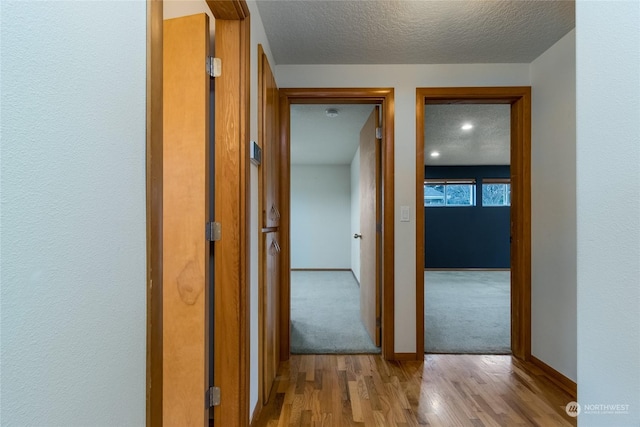 hallway with a textured ceiling and light hardwood / wood-style flooring