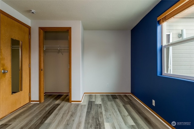 unfurnished bedroom with a textured ceiling, a closet, multiple windows, and hardwood / wood-style flooring