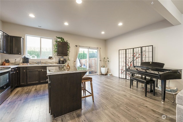 kitchen with hardwood / wood-style floors, a kitchen island, a kitchen breakfast bar, stainless steel range with electric stovetop, and dark brown cabinets