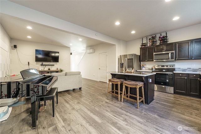 kitchen featuring appliances with stainless steel finishes, a kitchen island, light hardwood / wood-style floors, a kitchen breakfast bar, and dark brown cabinets