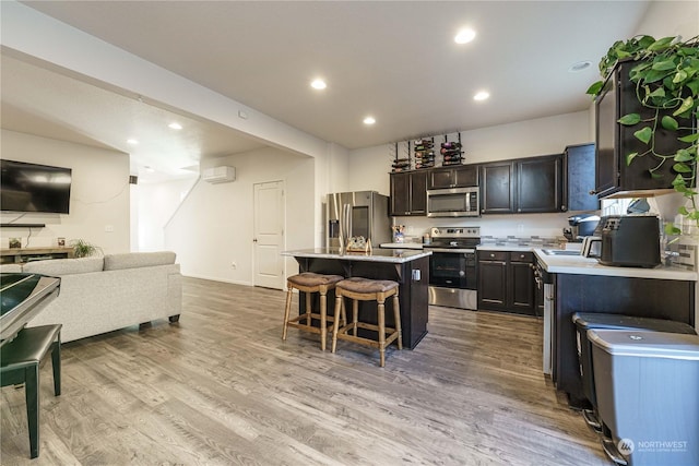 kitchen with dark brown cabinetry, appliances with stainless steel finishes, a kitchen island, light hardwood / wood-style flooring, and a breakfast bar area