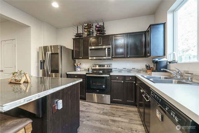 kitchen with dark brown cabinetry, stainless steel appliances, sink, a kitchen breakfast bar, and light hardwood / wood-style flooring