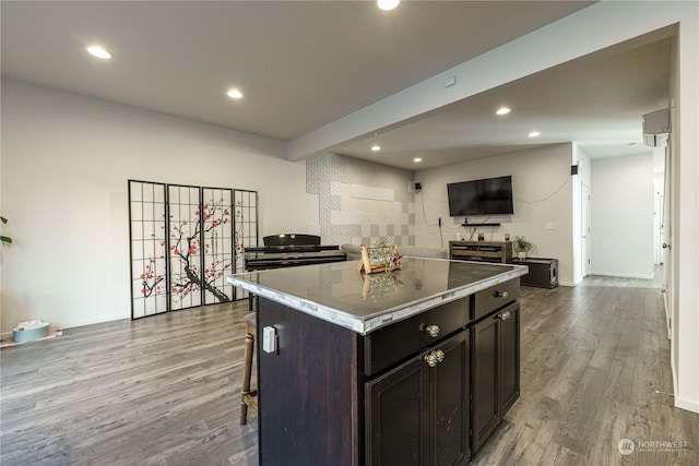 kitchen with a kitchen bar, wood-type flooring, dark brown cabinets, and a kitchen island