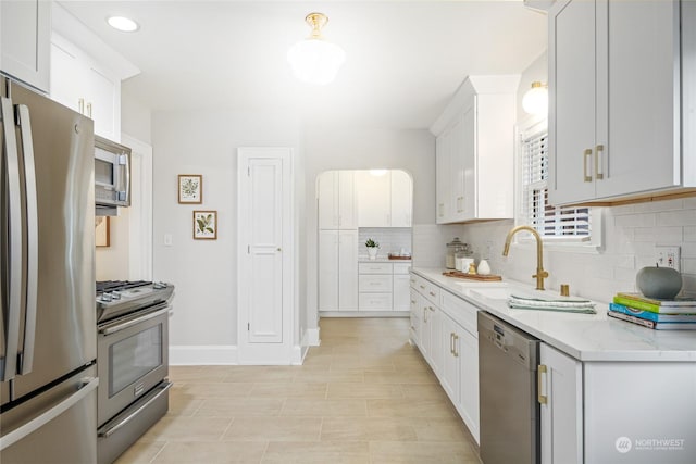 kitchen featuring light stone countertops, decorative backsplash, white cabinetry, appliances with stainless steel finishes, and sink