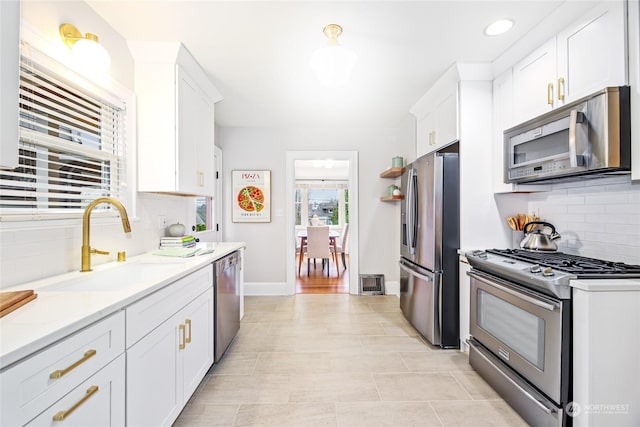 kitchen with appliances with stainless steel finishes, light stone counters, white cabinets, backsplash, and sink