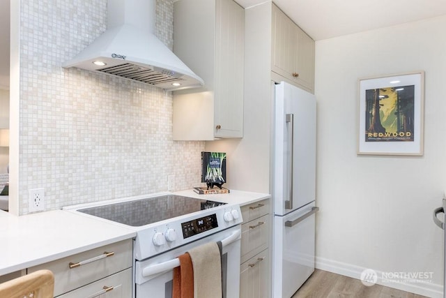 kitchen featuring wall chimney exhaust hood, tasteful backsplash, light wood-type flooring, high end white refrigerator, and range with electric cooktop