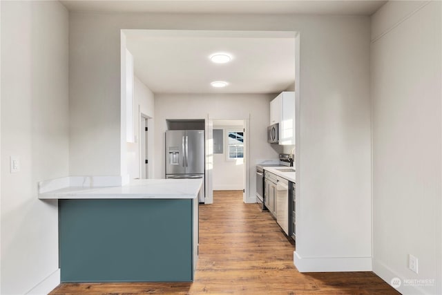 kitchen featuring appliances with stainless steel finishes, light stone countertops, kitchen peninsula, hardwood / wood-style flooring, and white cabinetry