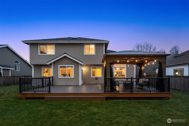 back house at dusk featuring a yard, a deck, and a gazebo