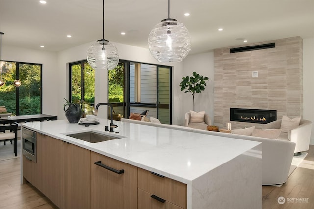 kitchen featuring stainless steel microwave, sink, hanging light fixtures, a fireplace, and a large island