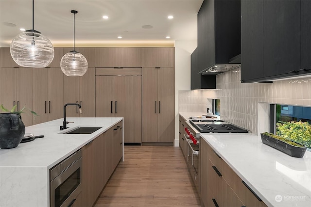 kitchen with light stone countertops, sink, stainless steel appliances, ventilation hood, and decorative light fixtures