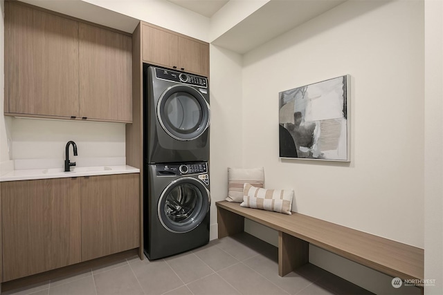 clothes washing area featuring stacked washer / dryer, sink, light tile patterned floors, and cabinets