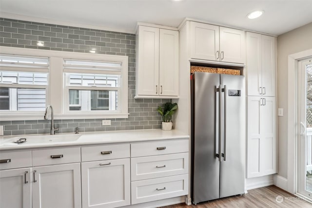 kitchen featuring sink, white cabinetry, light hardwood / wood-style floors, stainless steel refrigerator, and backsplash