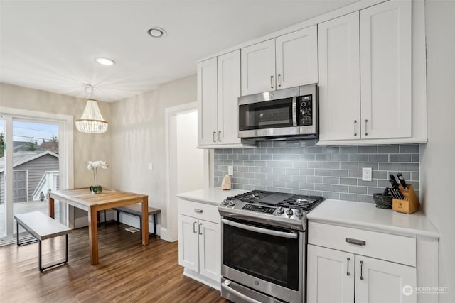 kitchen with stainless steel appliances, decorative light fixtures, white cabinetry, decorative backsplash, and dark wood-type flooring