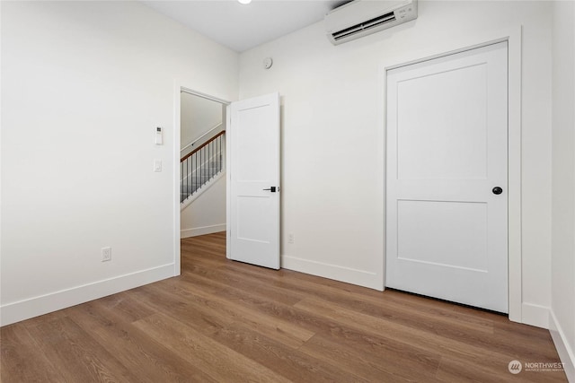 unfurnished bedroom with a closet, wood-type flooring, and a wall mounted air conditioner