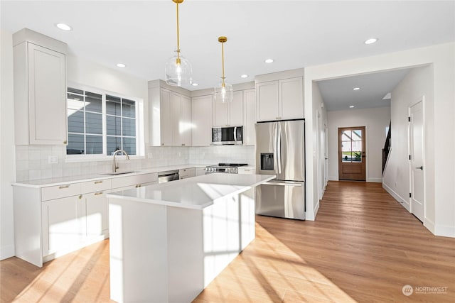 kitchen featuring appliances with stainless steel finishes, a center island, sink, hanging light fixtures, and light wood-type flooring