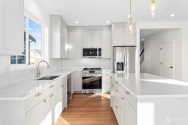 kitchen with a kitchen island, sink, white cabinetry, hanging light fixtures, and stainless steel appliances