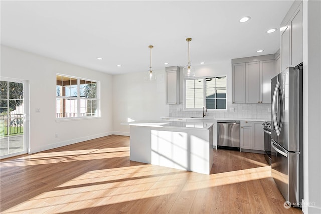 kitchen with appliances with stainless steel finishes, decorative backsplash, hanging light fixtures, light wood-type flooring, and gray cabinetry