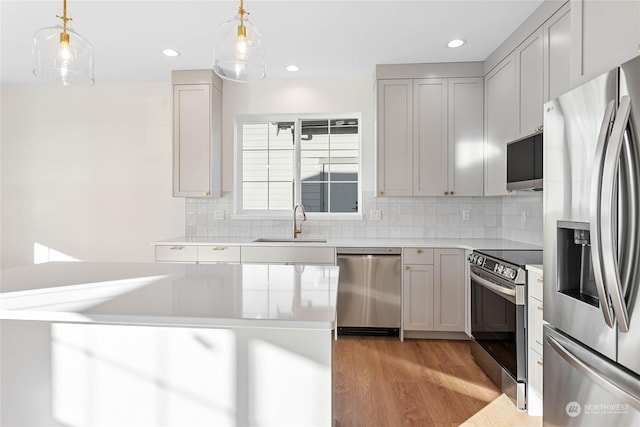 kitchen with gray cabinets, stainless steel appliances, light wood-type flooring, pendant lighting, and sink