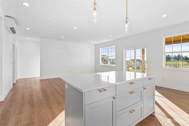 kitchen with light hardwood / wood-style floors, gray cabinets, a wall unit AC, decorative light fixtures, and a kitchen island