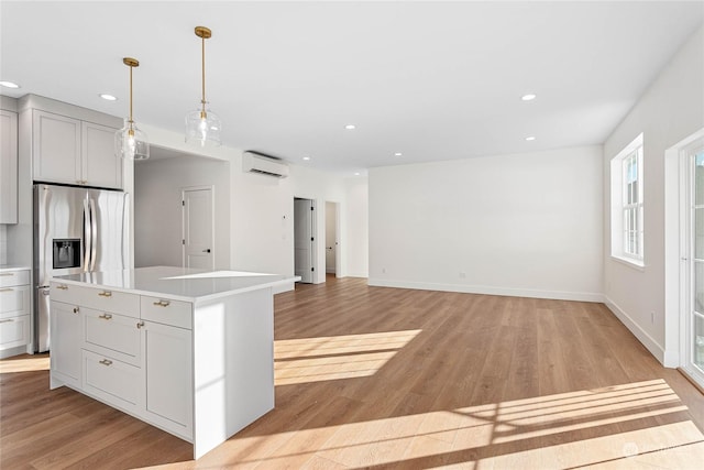 kitchen featuring a wall mounted AC, a center island, light hardwood / wood-style flooring, hanging light fixtures, and stainless steel fridge