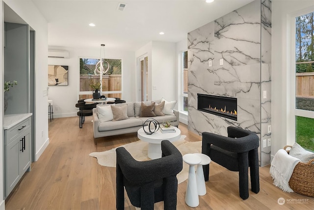 living room with light wood-type flooring, a high end fireplace, and a wall mounted air conditioner