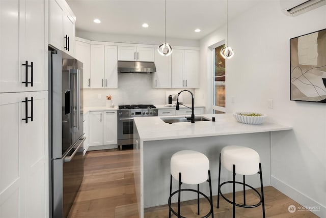 kitchen featuring decorative light fixtures, an AC wall unit, sink, white cabinetry, and high end appliances