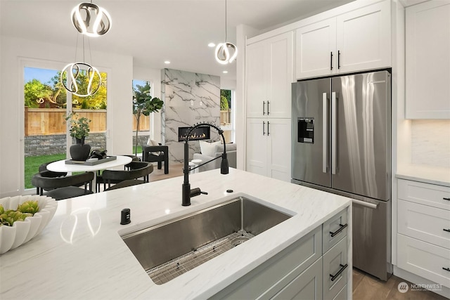 kitchen featuring light stone countertops, decorative light fixtures, white cabinetry, sink, and stainless steel fridge with ice dispenser