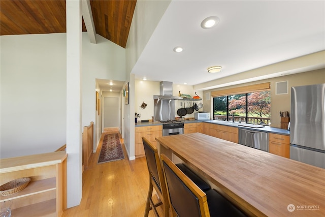 kitchen with light brown cabinetry, stainless steel appliances, exhaust hood, lofted ceiling with beams, and light hardwood / wood-style flooring