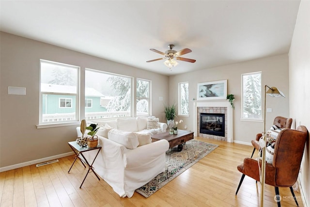 living room with a tile fireplace, plenty of natural light, ceiling fan, and light hardwood / wood-style floors