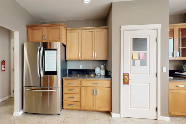 kitchen featuring stainless steel refrigerator, light tile patterned floors, and dark stone countertops