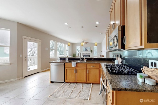 kitchen featuring sink, light tile patterned floors, appliances with stainless steel finishes, dark stone countertops, and decorative light fixtures