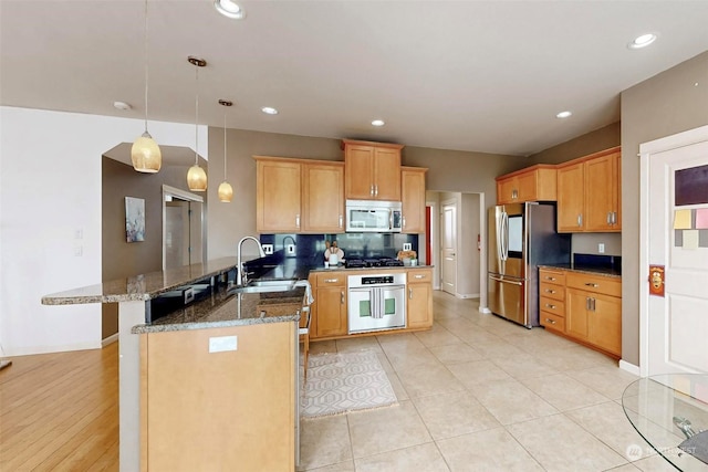 kitchen with sink, dark stone countertops, stainless steel appliances, decorative light fixtures, and kitchen peninsula