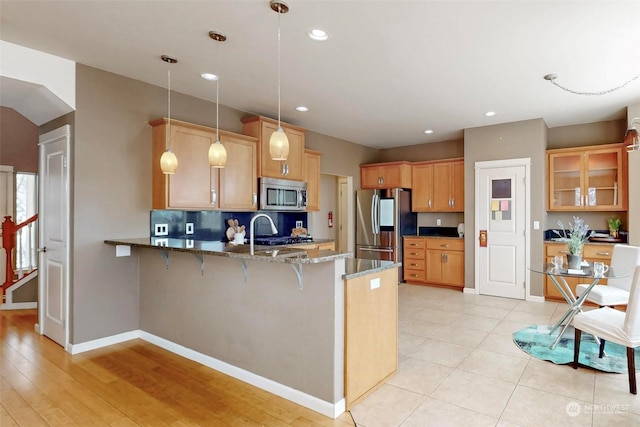 kitchen featuring stone countertops, a kitchen breakfast bar, kitchen peninsula, pendant lighting, and stainless steel appliances