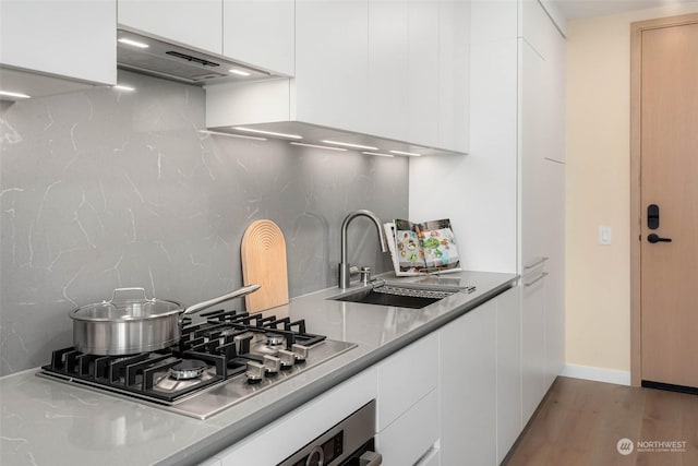 kitchen with appliances with stainless steel finishes, tasteful backsplash, white cabinetry, sink, and light wood-type flooring