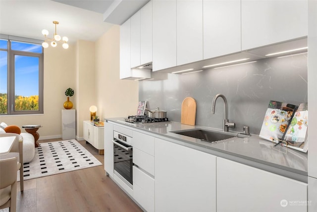 kitchen with pendant lighting, sink, light hardwood / wood-style flooring, appliances with stainless steel finishes, and white cabinetry