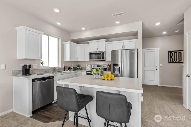 kitchen featuring light carpet, a kitchen breakfast bar, appliances with stainless steel finishes, a kitchen island, and white cabinetry