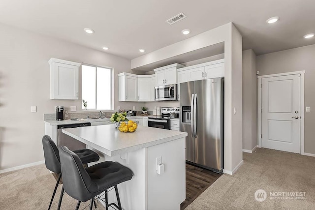 kitchen featuring white cabinetry, a center island, carpet floors, a kitchen bar, and appliances with stainless steel finishes