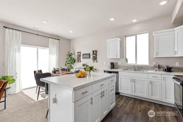 kitchen featuring electric stove, sink, stainless steel dishwasher, a kitchen island, and white cabinetry