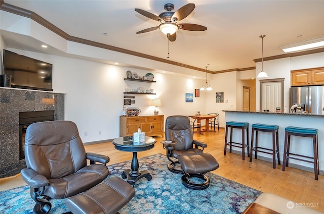 living room featuring ceiling fan, light wood-type flooring, crown molding, and a fireplace