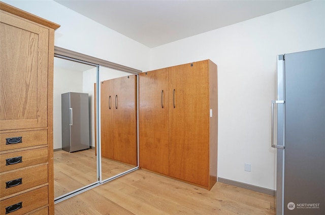 unfurnished bedroom featuring light hardwood / wood-style floors, stainless steel fridge, and a closet