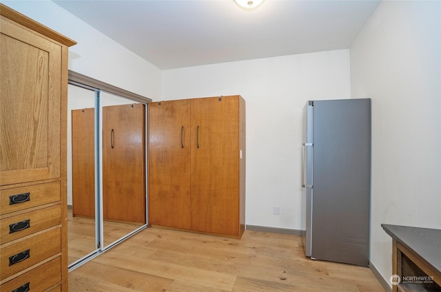 bedroom with light hardwood / wood-style floors, a closet, and stainless steel refrigerator