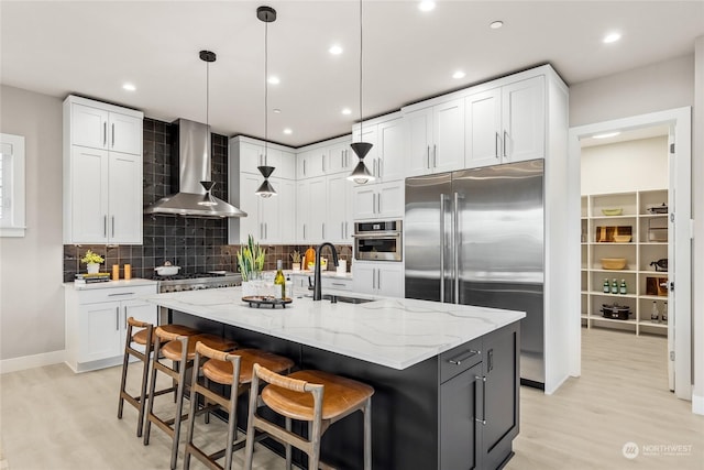 kitchen featuring appliances with stainless steel finishes, wall chimney range hood, and white cabinets