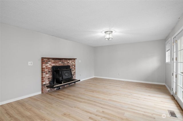 unfurnished living room with a wood stove, a textured ceiling, and light hardwood / wood-style flooring