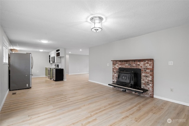 unfurnished living room featuring light wood-type flooring, a wood stove, and a textured ceiling